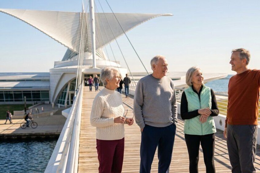 A wooden boardwalk with people walking, a modern building with a unique roof design, and a body of water in the background. 5