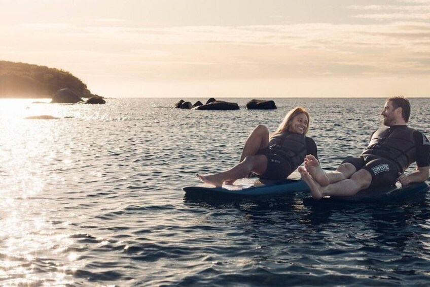 Two people on a surfboard in calm ocean waters with a sunset in the background. 2