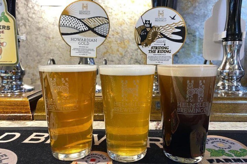 Three glasses of beer with tap handles labeled 'Howardian Gold' and 'Striding the Riding.' 4