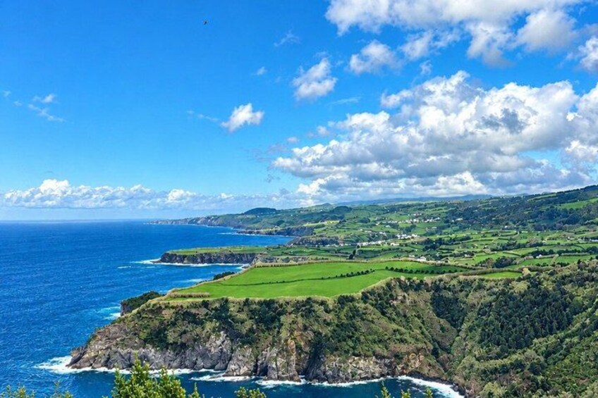 A coastal landscape with green fields, cliffs, and the ocean. 5