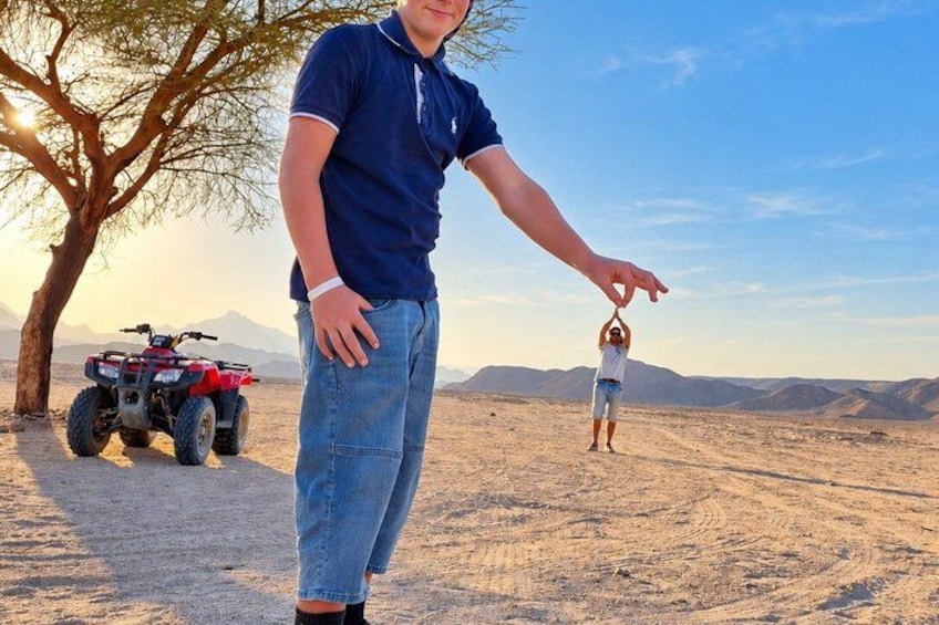 A person in a blue shirt and jeans, a child in a white shirt and shorts, and an ATV in a desert landscape with mountains in the background. 1