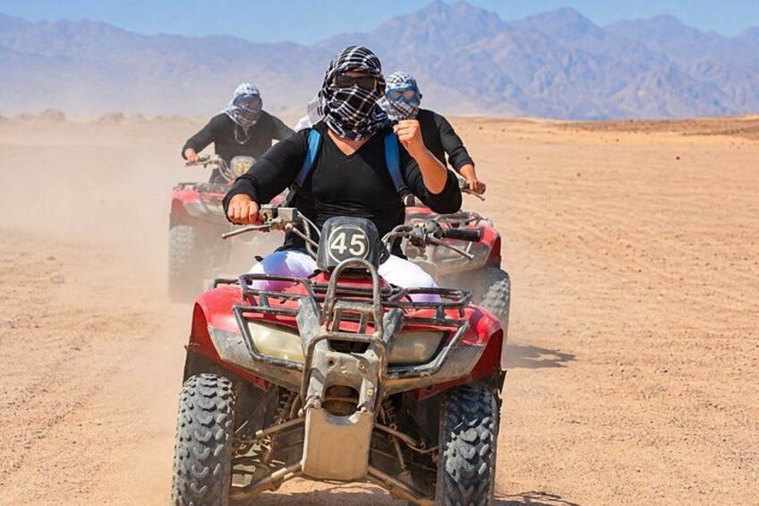 Two people riding atv's on a desert road with mountains in the background. 5