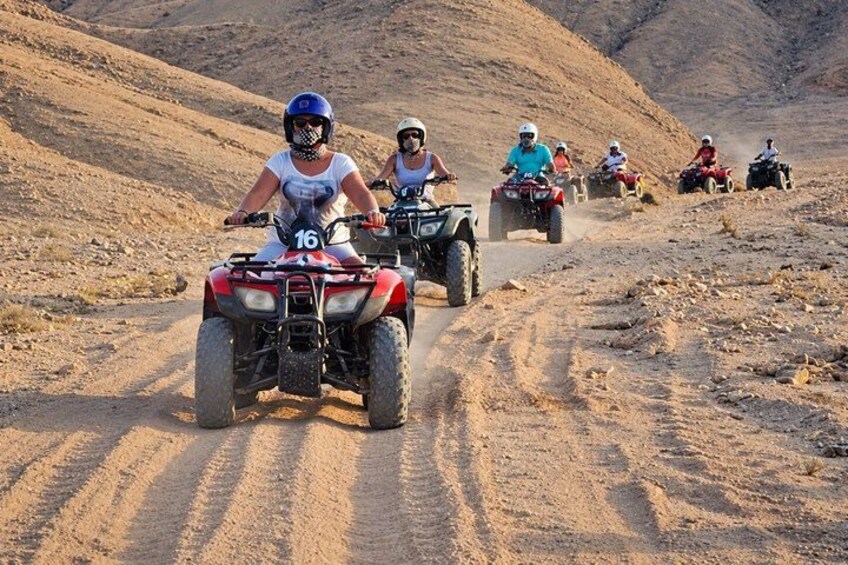 A group of people riding ATVs on a dirt road in a desert landscape. 3