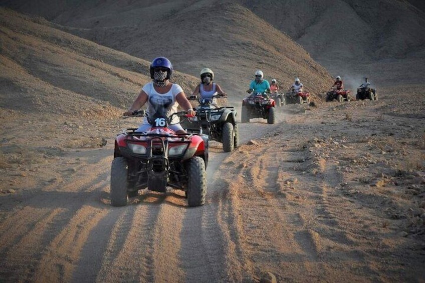 A group of people riding ATVs on a sandy trail in a desert landscape. 4