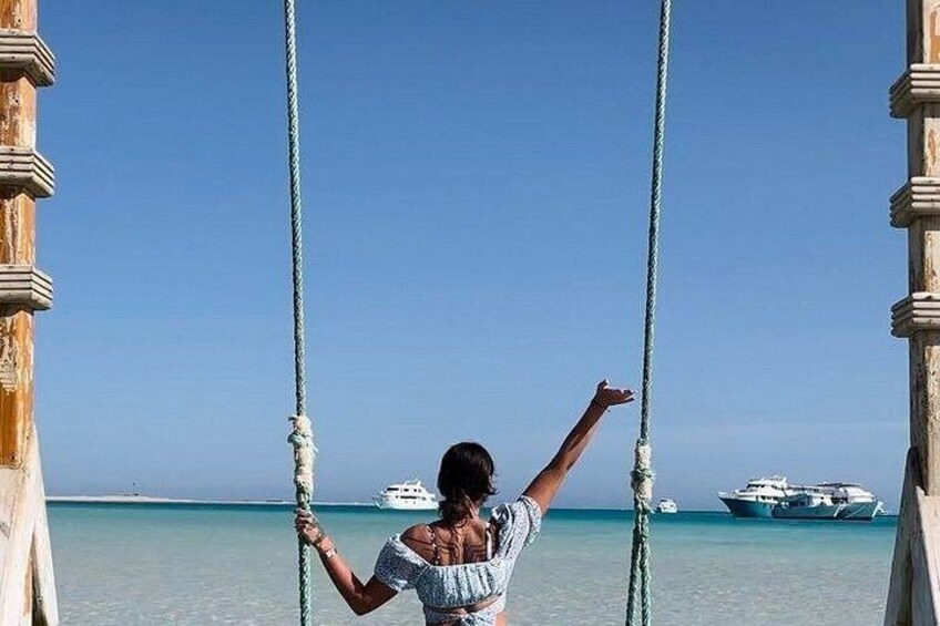 A person on a swing with ropes, a boat in the background, and a clear blue sky. 5