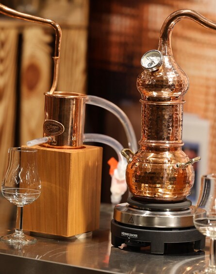 A copper still with a thermometer, a wooden box, and a glass on a counter. 4