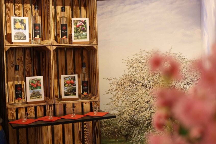 A wooden display with Hecht brand bottles and framed pictures of fruit trees. 3