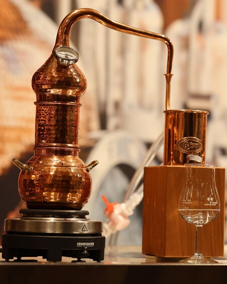 A copper distillation apparatus with a thermometer, a glass container, and a wooden box. 1