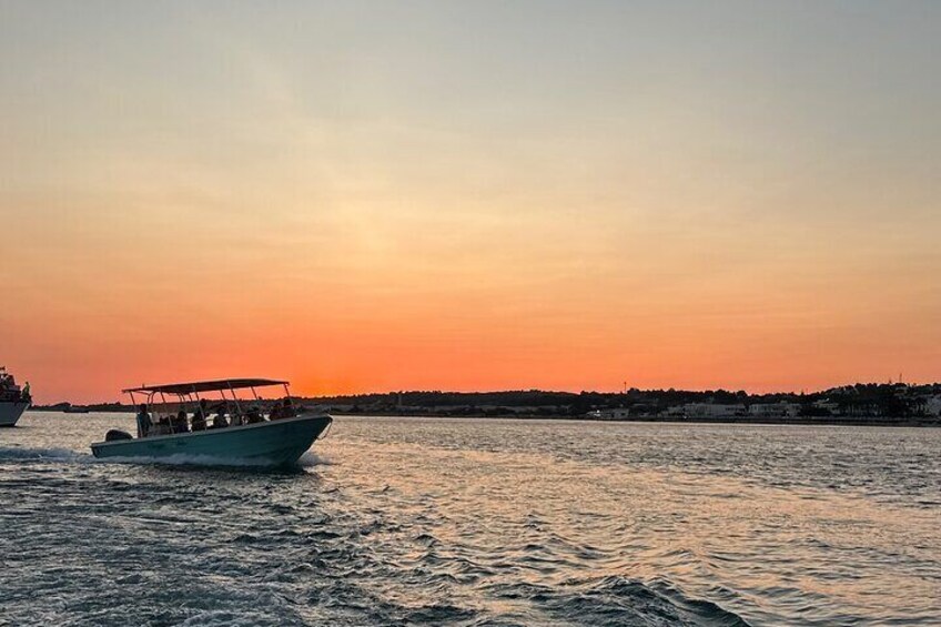 A boat on calm water during sunset with a city skyline in the background. 2