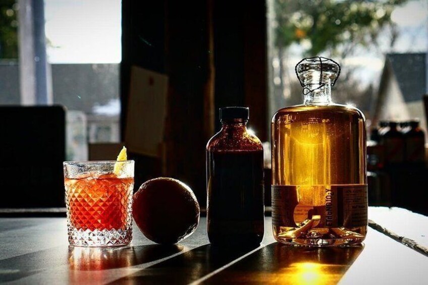 A whiskey bottle, a glass with a lemon, and a fruit on a table. 1