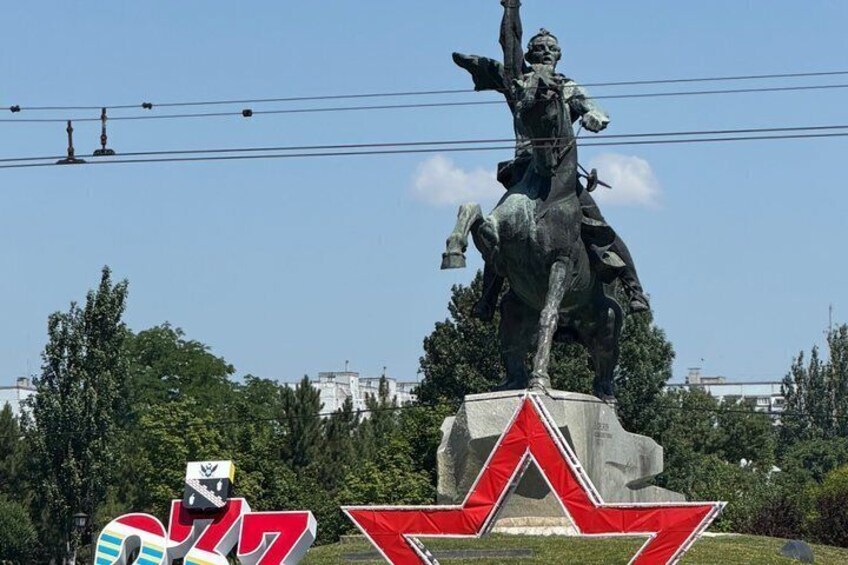A statue of a person on horseback, a red star emblem, and a building in the background. 3