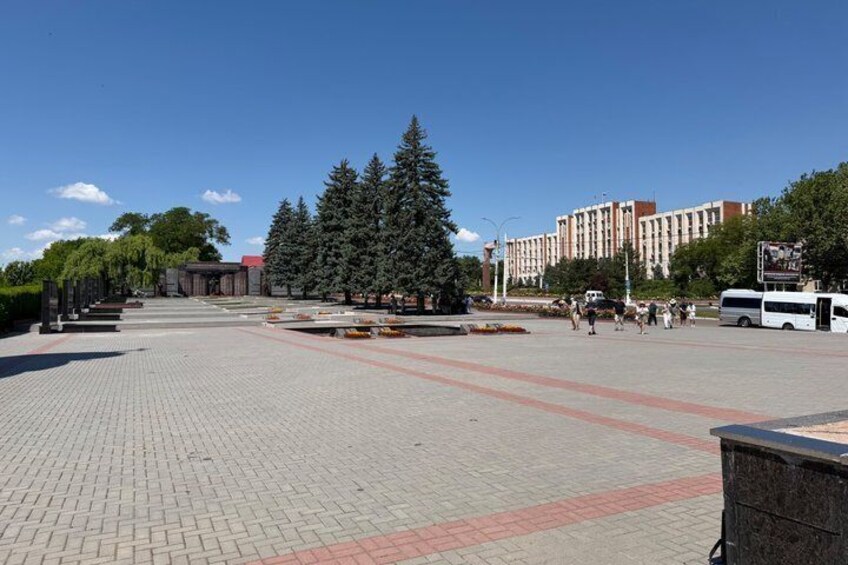 A paved plaza with trees, a bus, and a building in the background. 2