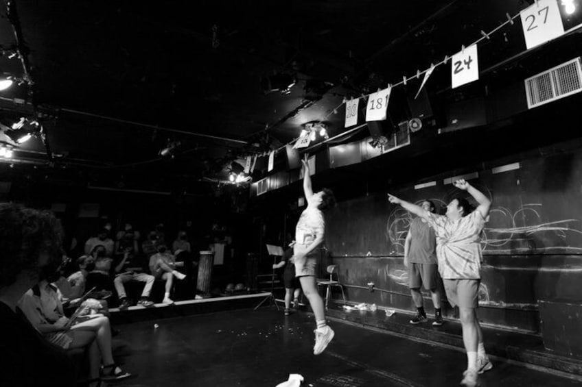 A dance performance with dancers on stage, audience seated, and graffiti on walls. 3