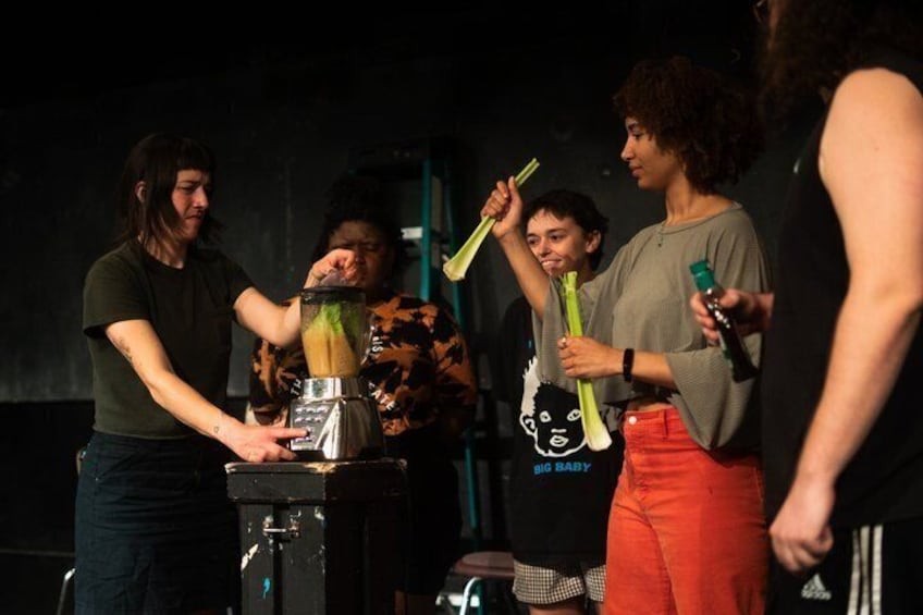 A group of people on a stage with a blender and green sticks. 2
