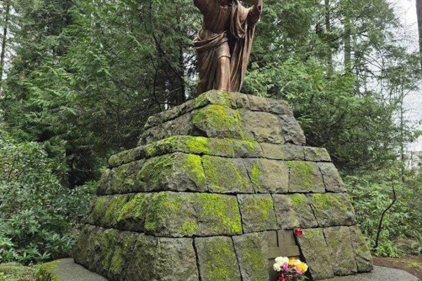 A stone statue on a moss-covered pedestal in a forest. 2