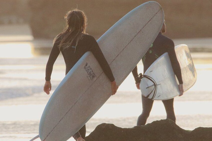 Two people carrying surfboards on a beach. 3