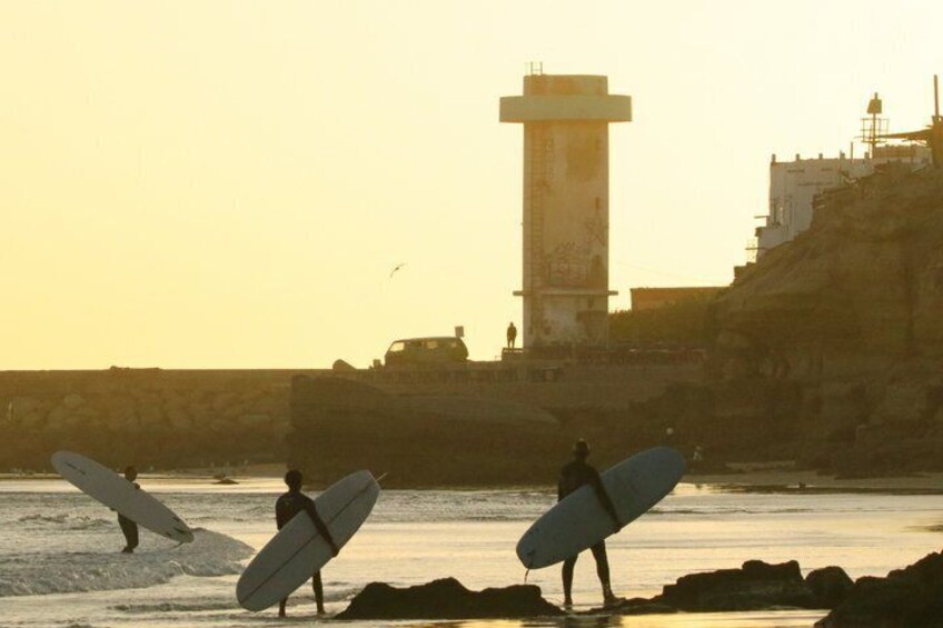 Surfers carrying boards on a beach with a lighthouse in the background. 2