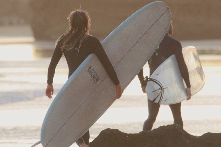 Two people carrying surfboards on a beach. 3