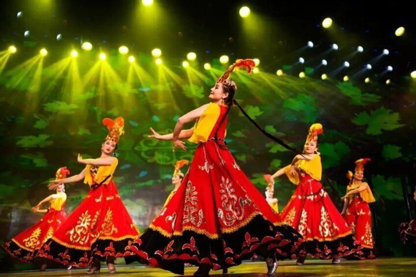 A dance performance with dancers in red and yellow costumes on a stage with green foliage backdrop. 2