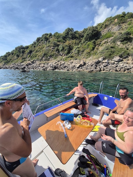 A group of people on a boat with a rocky shoreline and greenery in the background. 3