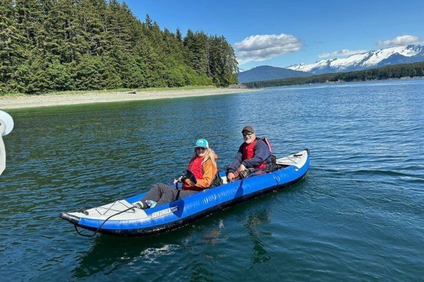 Two people in a blue kayak on a calm lake with forested shores and mountains in the background. 5
