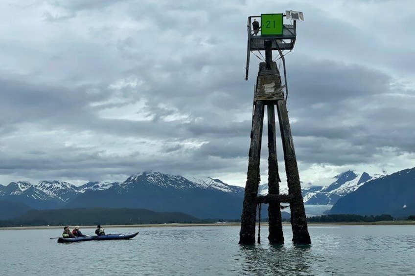 A tall structure with a green sign, a kayak with two people, and a mountainous landscape in the background. 3