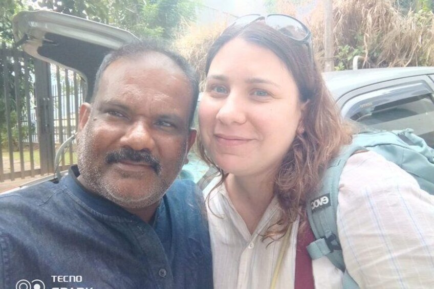 Two people taking a selfie with a car and a gated area in the background. 2