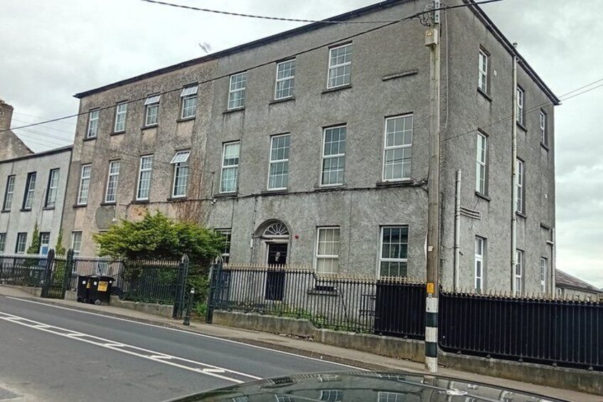 A multi-story building with a black fence in front, a clear road, and a parked car. 5