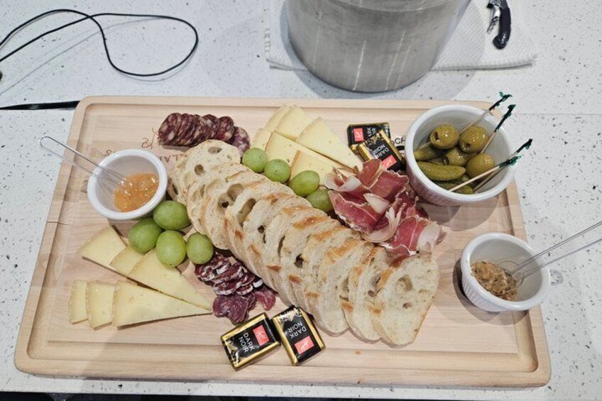A charcuterie board with cheese, cured meats, olives, and bread on a wooden cutting board. 2