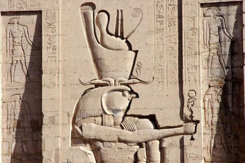 A carved relief of a seated figure with a staff, surrounded by hieroglyphs on a stone wall. 5