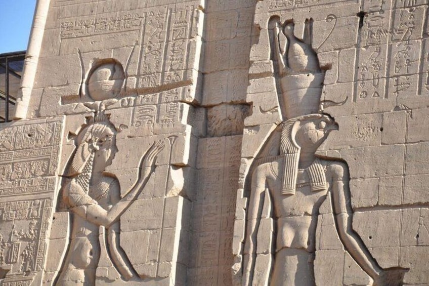 Ancient Egyptian hieroglyphs and statues on a stone wall. 3