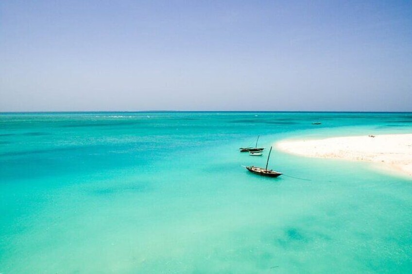 A turquoise sea with a sandy beach and two boats. 1