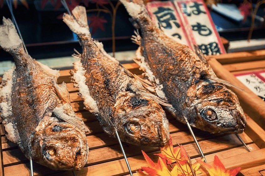 Three whole fish on skewers, displayed on a wooden surface with a decorative leaf arrangement. 4