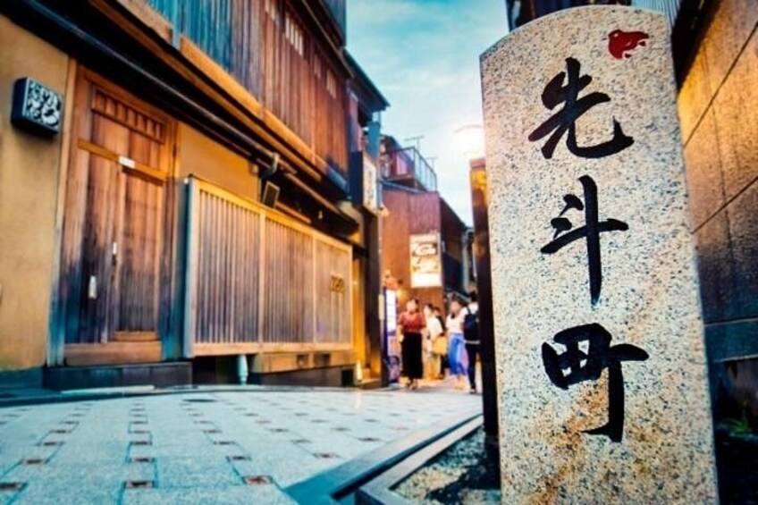 A traditional Japanese street with wooden buildings, a stone pillar with Japanese characters, and a clear sky. 3