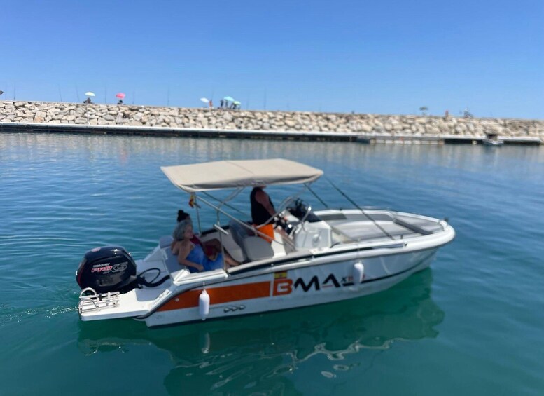 A small motorboat with a canopy, anchored near a rocky shore with people on the beach. 2