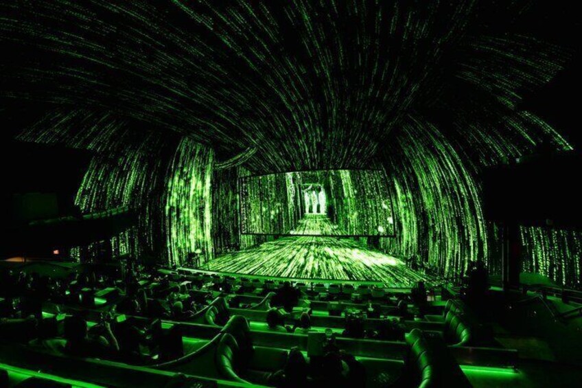 An indoor venue with a stage and audience seating, illuminated by green lighting. 5
