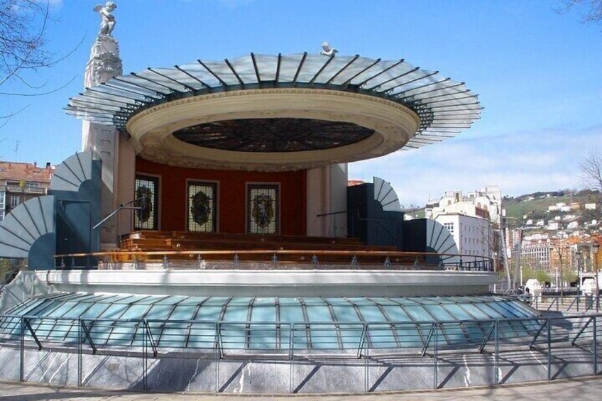 A circular building with a glass roof, a stage, and a fountain in front. 4