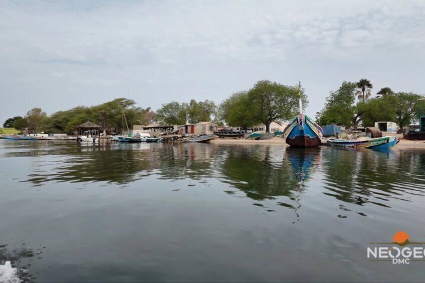A calm river with boats docked along the shore, surrounded by trees and buildings. 1