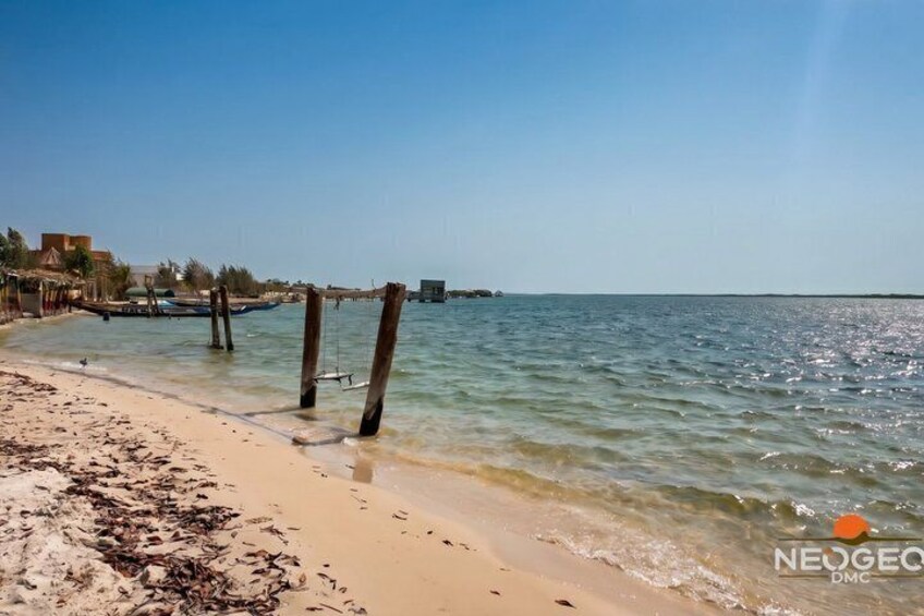 A beach with clear water, a sandy shore, and a pier extending into the sea. 2