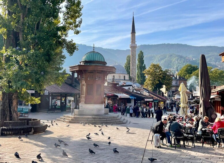 A public square with a central monument, surrounding shops, and a mosque with a minaret in the background. 2
