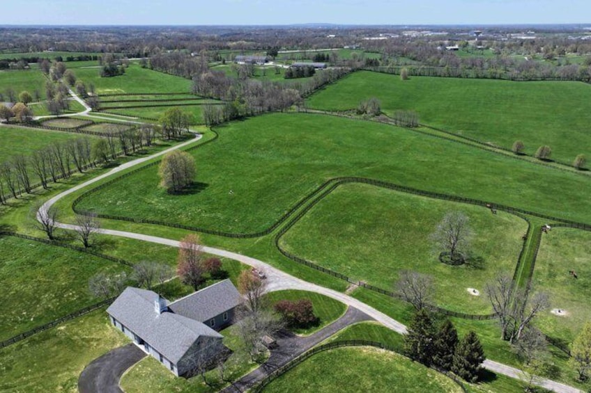 An aerial view of a large green field with a winding path, a barn, and a few scattered trees. 3