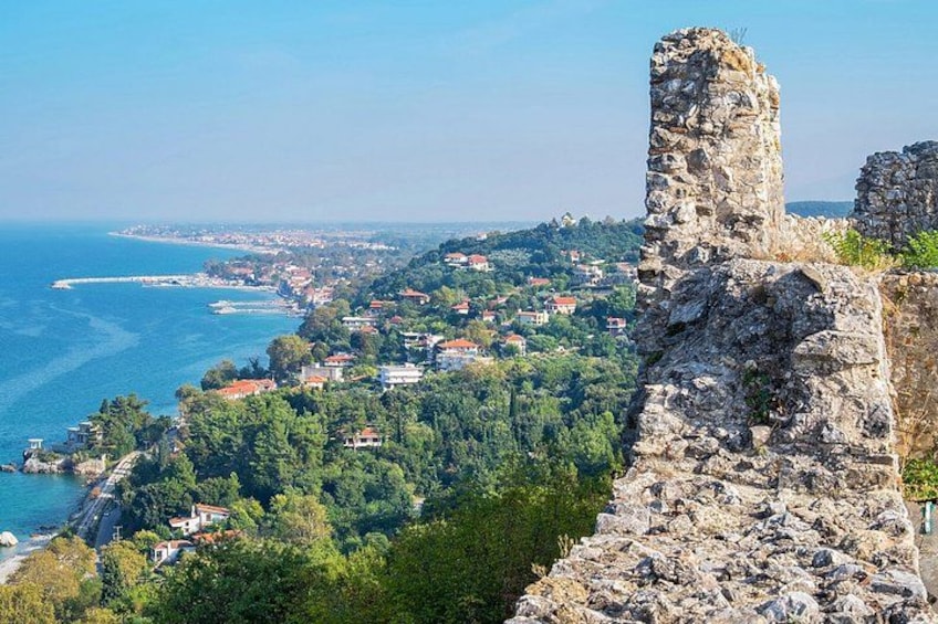 A coastal town with a prominent stone ruin, lush greenery, and a clear view of the sea. 2