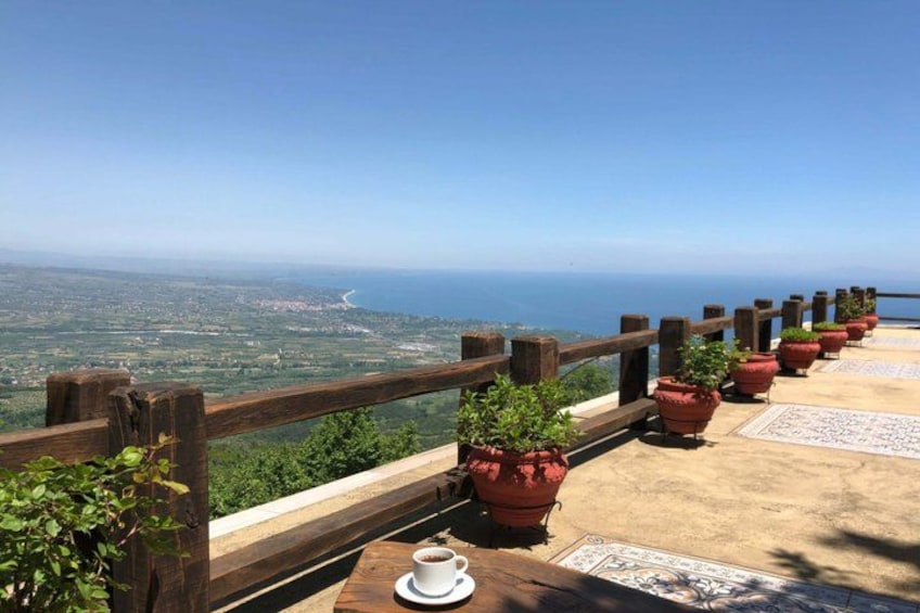 A wooden railing overlooking a coastal landscape with potted plants and a table with a cup. 3