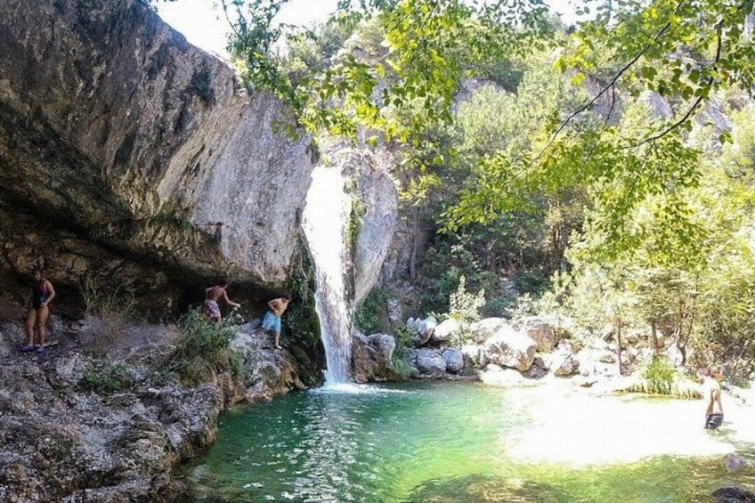 A natural landscape with a waterfall, rocky terrain, and a clear pool of water. 1