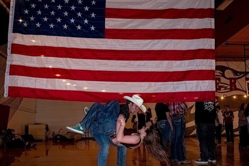 A large American flag, a person in a cowboy hat, and a crowd of people in an indoor setting. 3