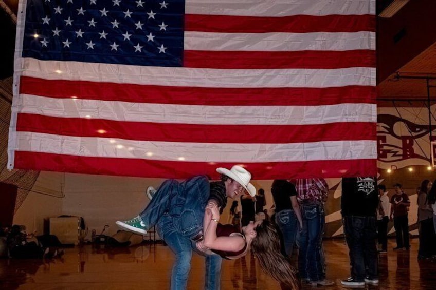 A large American flag, a person in a cowboy hat, and a crowd in an indoor setting. 2