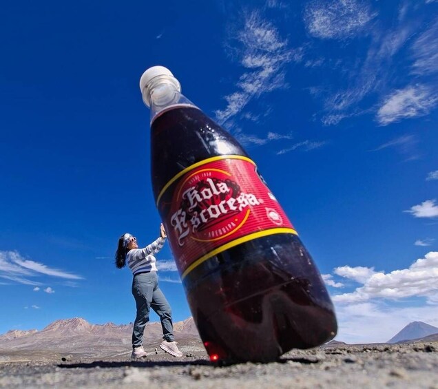 A person standing next to a large bottle of Coca-Cola in a desert landscape. 3