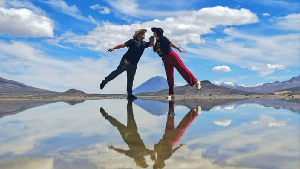 Two people dancing on a reflective surface with mountains in the background. 5