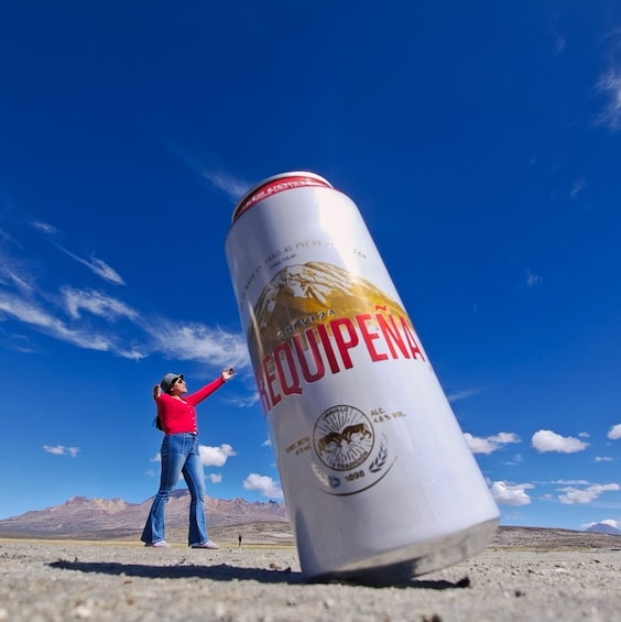 A person pointing at a large can of beer in a desert landscape. 2