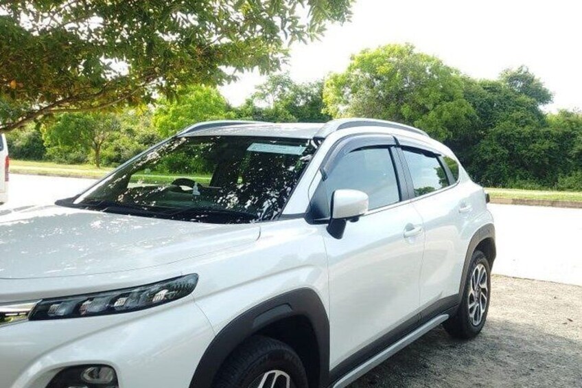 A white SUV parked on a gravel surface with trees in the background. 3